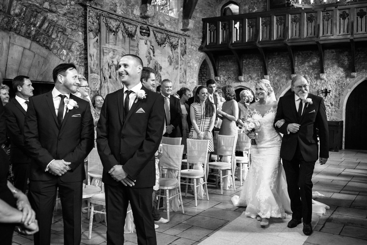 Black and white photograph of Lexy walking up the aisle in Allington Castle on her wedding day