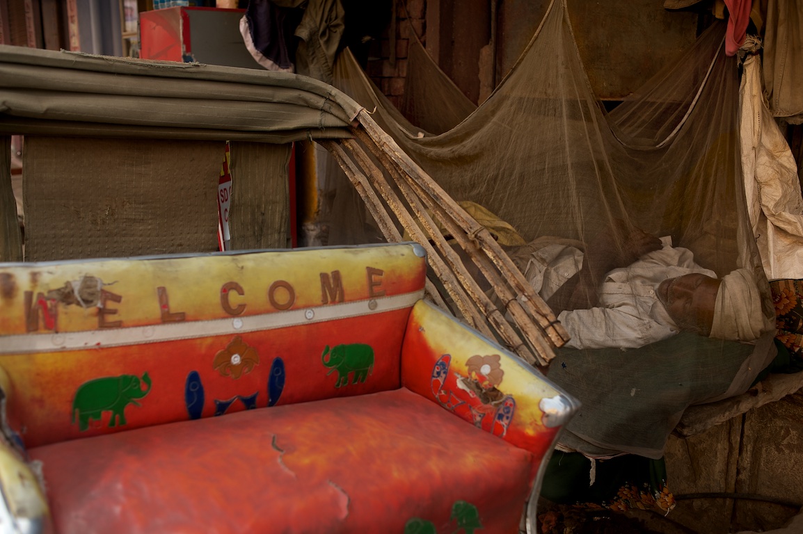 Photograph of rickshaw driver asleep by his rickshaw in India