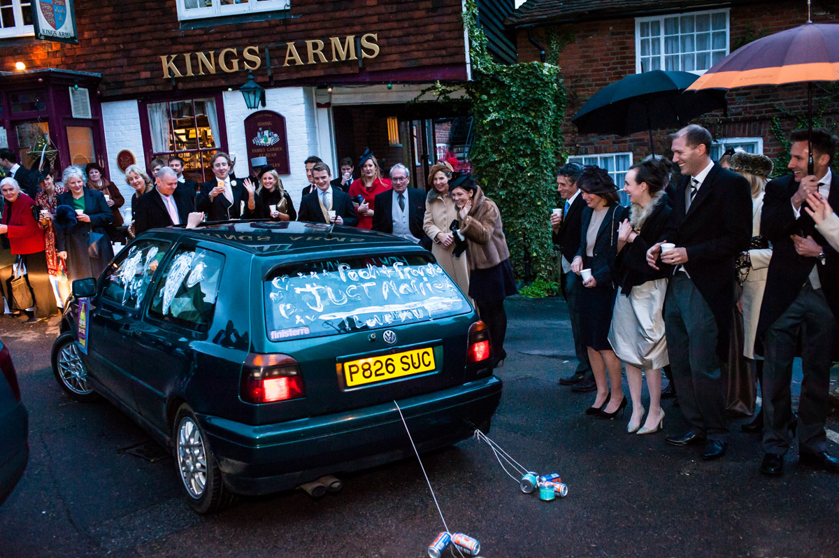 Photograph of wedding guests waving off newly weds leaving in their car