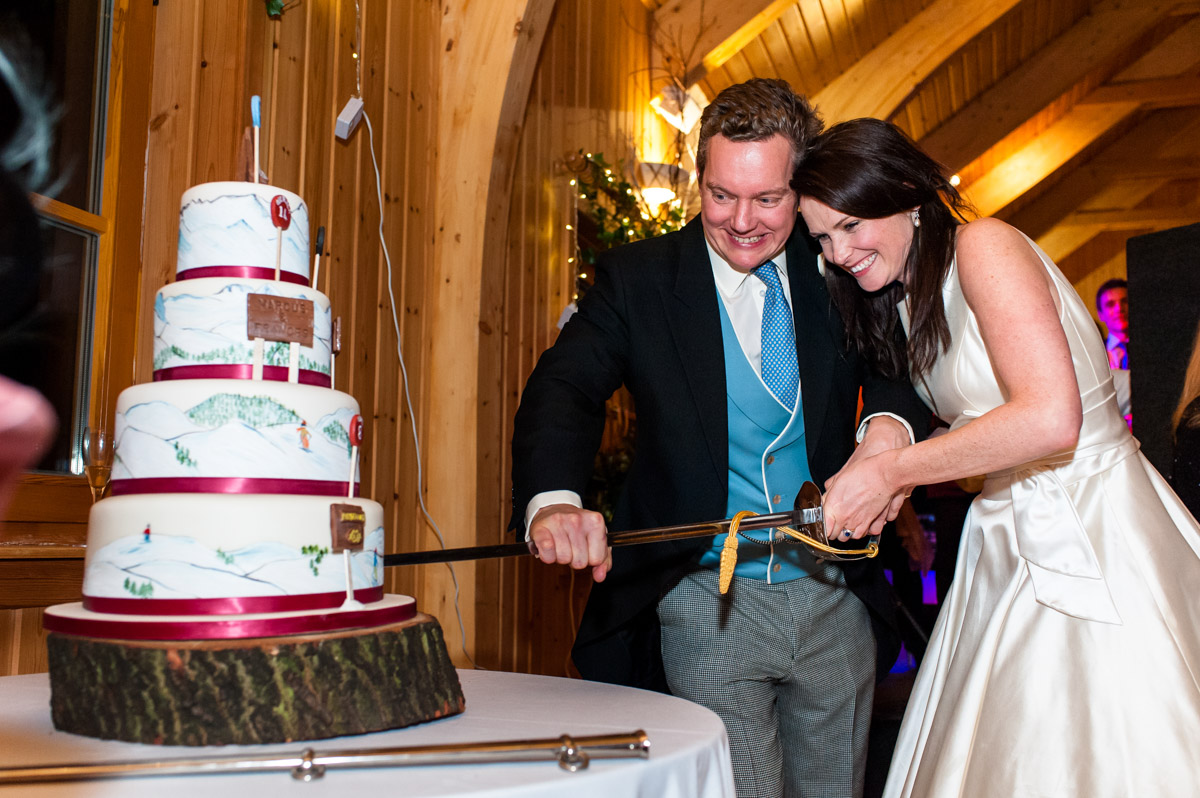 Marcus and Frances are photographed cutting their wedding cake with ceremonial sword