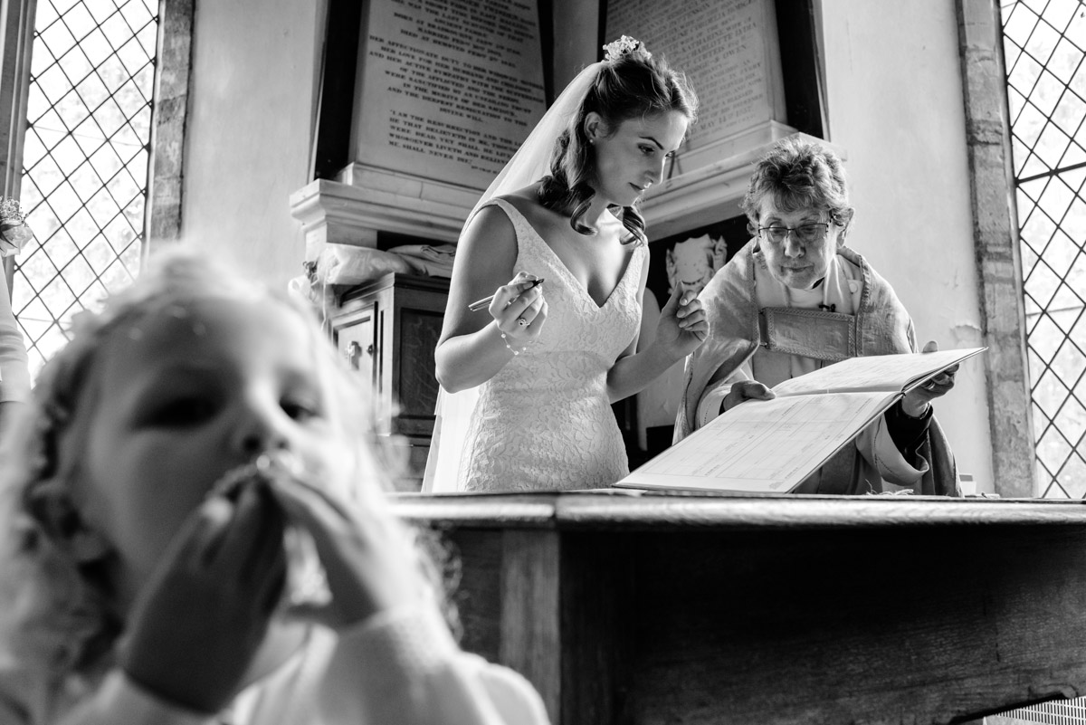 Black and white photograph of Ellie and Vicar signing Kent wedding register