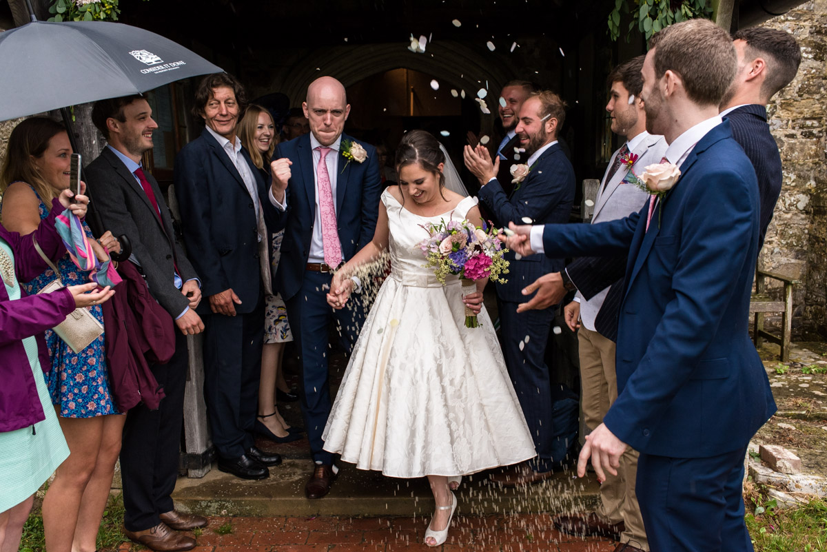 Photograph of Emily and Tom leaving the church under confetti after their wedding ceremony
