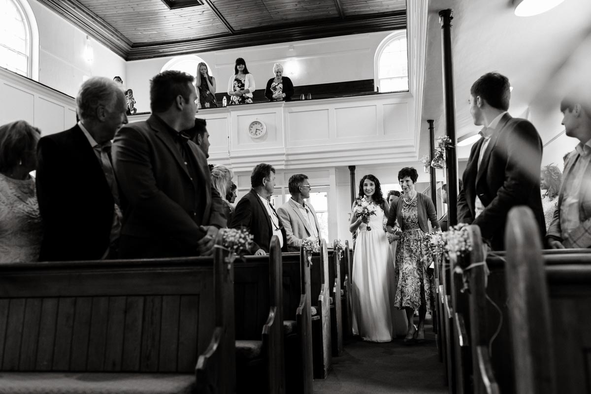 Black and white photograph of Claire and her mum walking down the aisle on her wedding day
