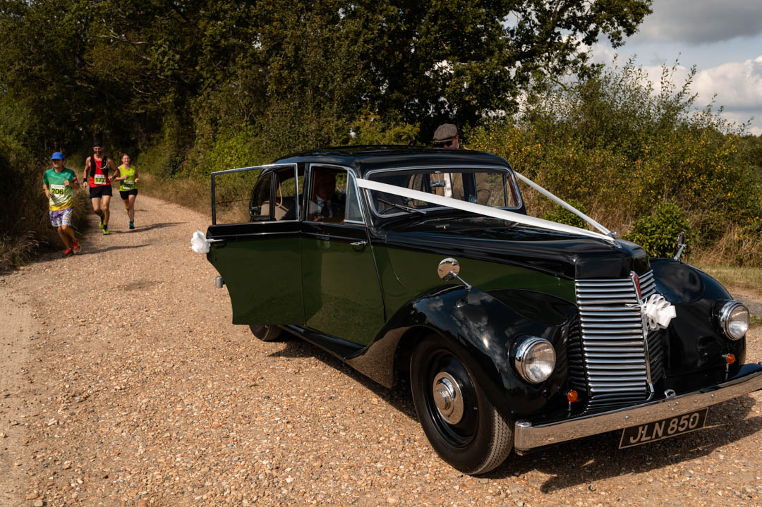 Runners pass Fiona as she exits wedding car at The Cherry Barn in Peasmarsh