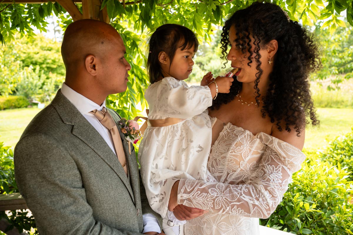 Daughter of bride giving mum a biscuit after the wedding ceremony at The Secret garden in Kent.